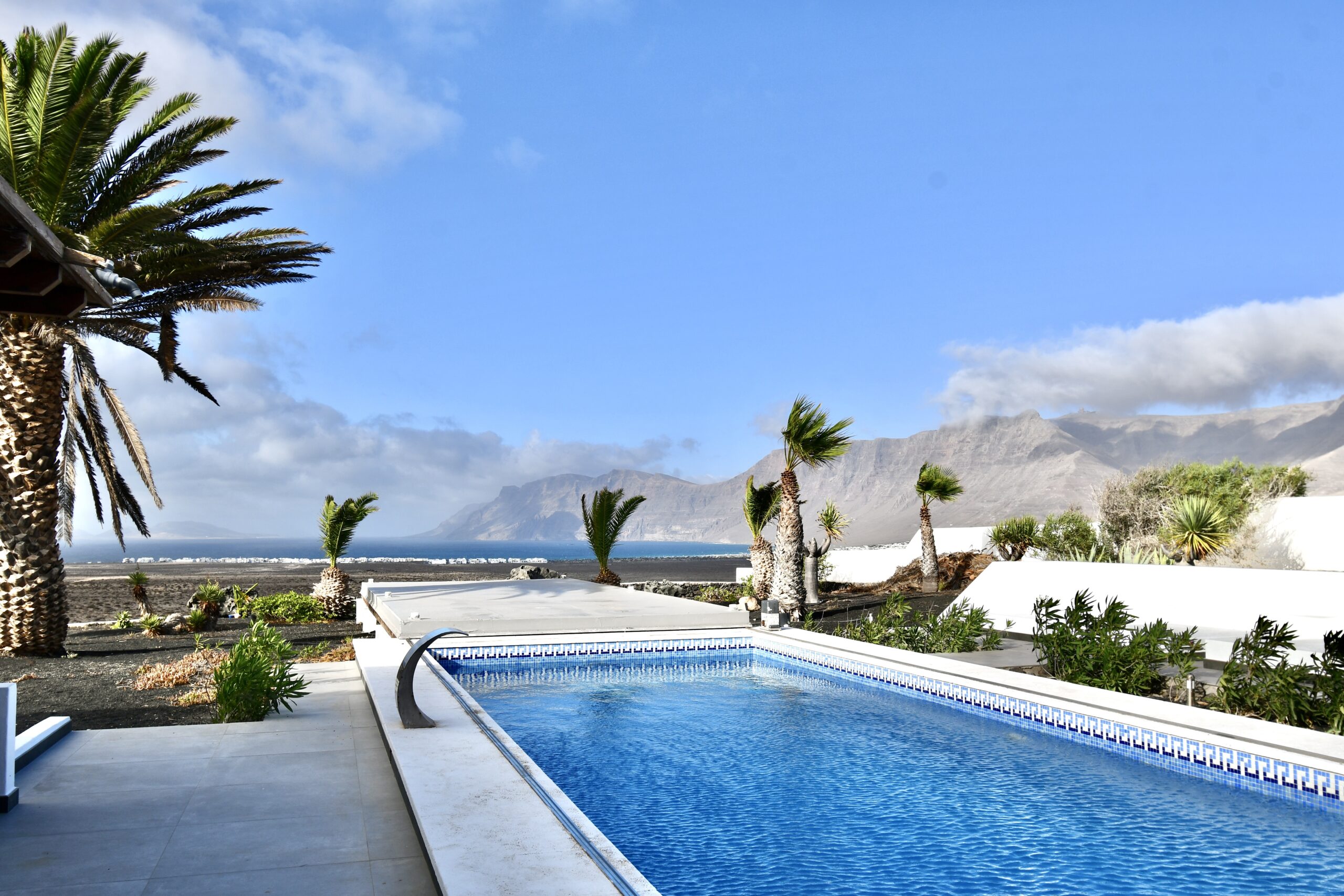La piscina de la villa entre palmeras, con vistas al océano y al risco